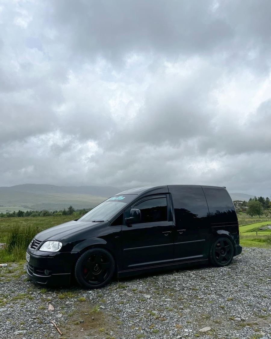 Finished black Caddy, lowered on black wheels, parked in the countryside